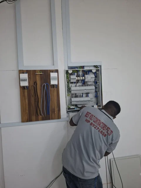 Best Volt electrician terminating an open distribution board beside a timber meter board in a Singapore commercial unit.