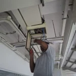 Best Volt on a ladder at the overhead ceiling enclosure above the Audanis Bakes shopfront, cover open and glass below.