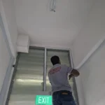 Green EXIT sign at a security grille with fluorescent lighting, escape lighting and shutter-head electrics by Best Volt at the Audanis Bakes fit-out.
