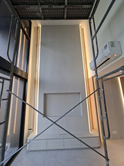 Feature wall by Best Volt in a double-volume Singapore condominium, recessed niche, vertical LED cove on both sides, and a low cabinet below.