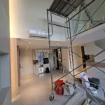 Scaffold rising to the mezzanine in a double-volume condominium, high-wall air-con and kitchen beyond, during a Best Volt feature-lighting installation.