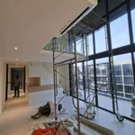 Floor-to-ceiling glazing, balcony, and scaffold in a double-volume condominium during Best Volt feature-lighting works, with a high-wall air-con.