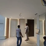 Vertical LED strip lit on a wood-slat wall, loose cable still dropping from the ceiling, during a Best Volt feature-lighting fit-out.