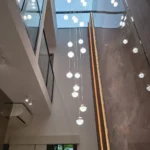 Double-height residence with a glass-globe bubble chandelier, skylight, marble wall, and gold linear LED, installed by Best Volt.
