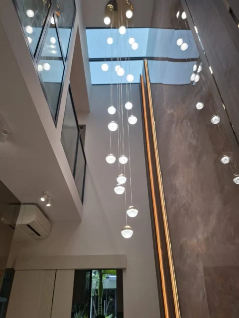 Double-height residence with a glass-globe bubble chandelier, skylight, marble wall, and gold linear LED, installed by Best Volt.