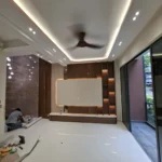 Wide living room with the cove ceiling lit, a ceiling fan, and a pendant against the marble wall, during a Best Volt feature-lighting fit-out.