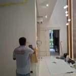 Partition chase with yellow tape and a cable drop, chandelier hall and gold LED of the same residence visible behind, by Best Volt.