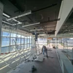 Linear light being mounted from a ladder on a black office ceiling, glass partition behind, by Best Volt.