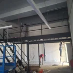 Best Volt crew on a black steel mezzanine, ladder and scissor lift in frame, during a mezzanine lighting installation.