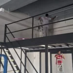 Trunking and conduit run along the top of a steel mezzanine by Best Volt, with a ladder in use on the floor below.