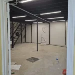 Rows of tube lights switched on in an empty unit, mezzanine and stair in frame, completed by Best Volt.