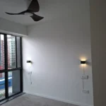 Finished residential lighting by Best Volt, a dark ceiling fan with light and two black wall sconces switched on beside a large window.