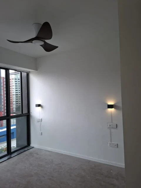 Finished residential lighting by Best Volt, a dark ceiling fan with light and two black wall sconces switched on beside a large window.