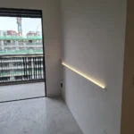 Horizontal wall-wash LED and a socket beside a balcony in a new-build residence, crane visible outside, installed by Best Volt.