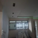 Downlight openings set out on a ceiling with a green laser line and a window grille, a Best Volt lighting-layout method shot.