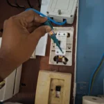Voltage tester lit on a Schneider 63A 30mA RCBO on an older timber panel, MEM isolator off below, during protection testing by Best Volt.